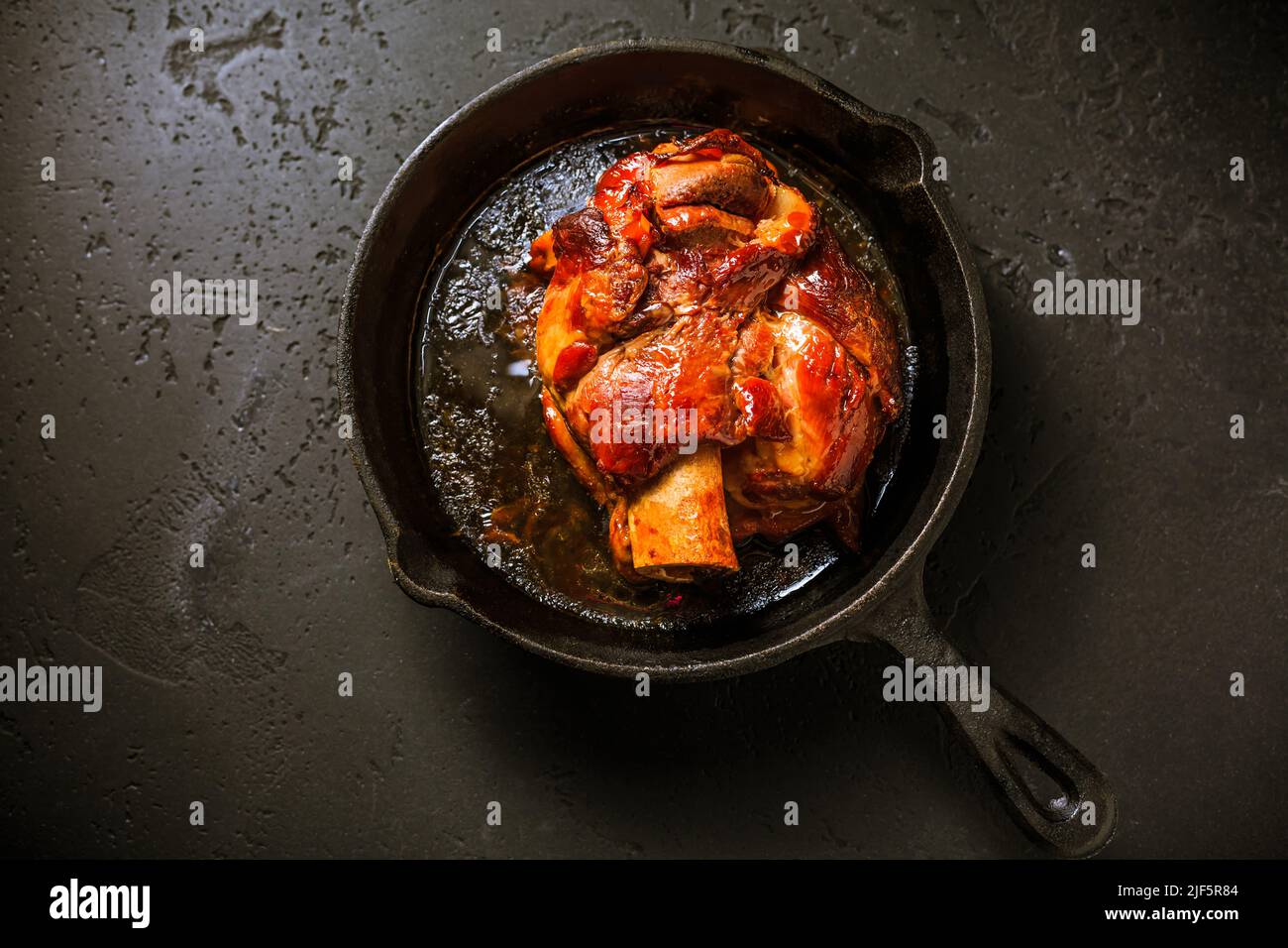 Cucina tradizionale tedesca - Pasta di maiale arrosto eisbein (Schweinshaxe) in padella di ferro su sfondo nero Foto Stock