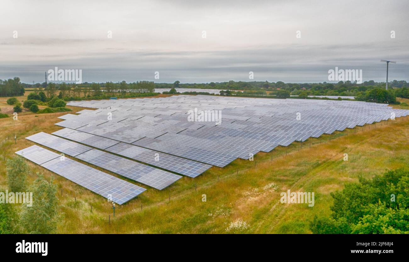 Un campo di pannelli solari in Essex, energia solare sostenibile, con turbine eoliche e cielo nuvoloso Foto Stock