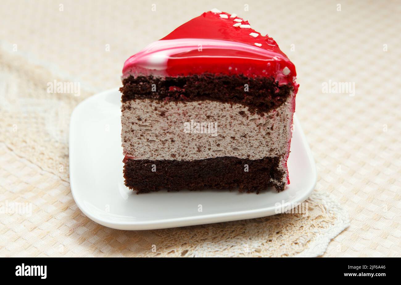 Una deliziosa torta dolce ricoperta di glassa rossa si trova in un piatto da dessert sul tavolo Foto Stock