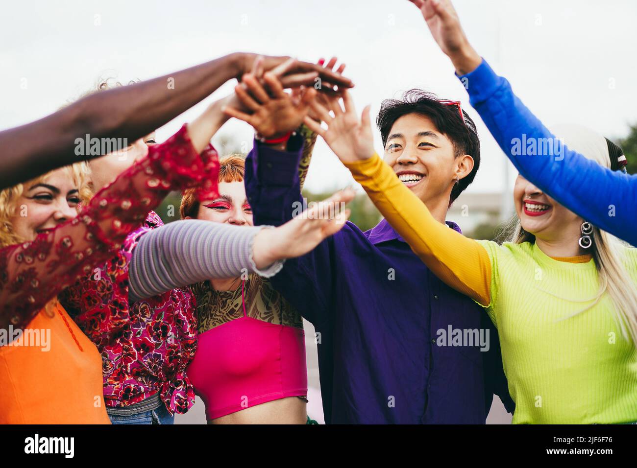 Giovani amici diversi che si divertono a impilare le mani all'aperto - Focus su ragazza con eyeshadow rosa Foto Stock