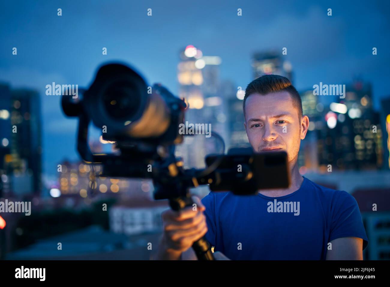 Uomo che filma con fotocamera e gimbal. Ritratto di videografo contro skyline urbano illuminato di notte. Foto Stock
