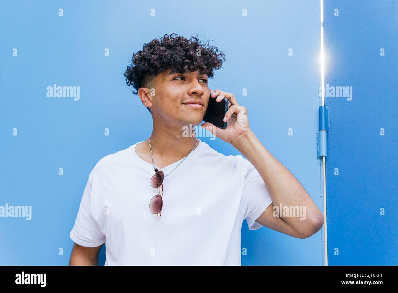 Maschio positivo su parete blu e parlare al telefono cellulare Foto Stock