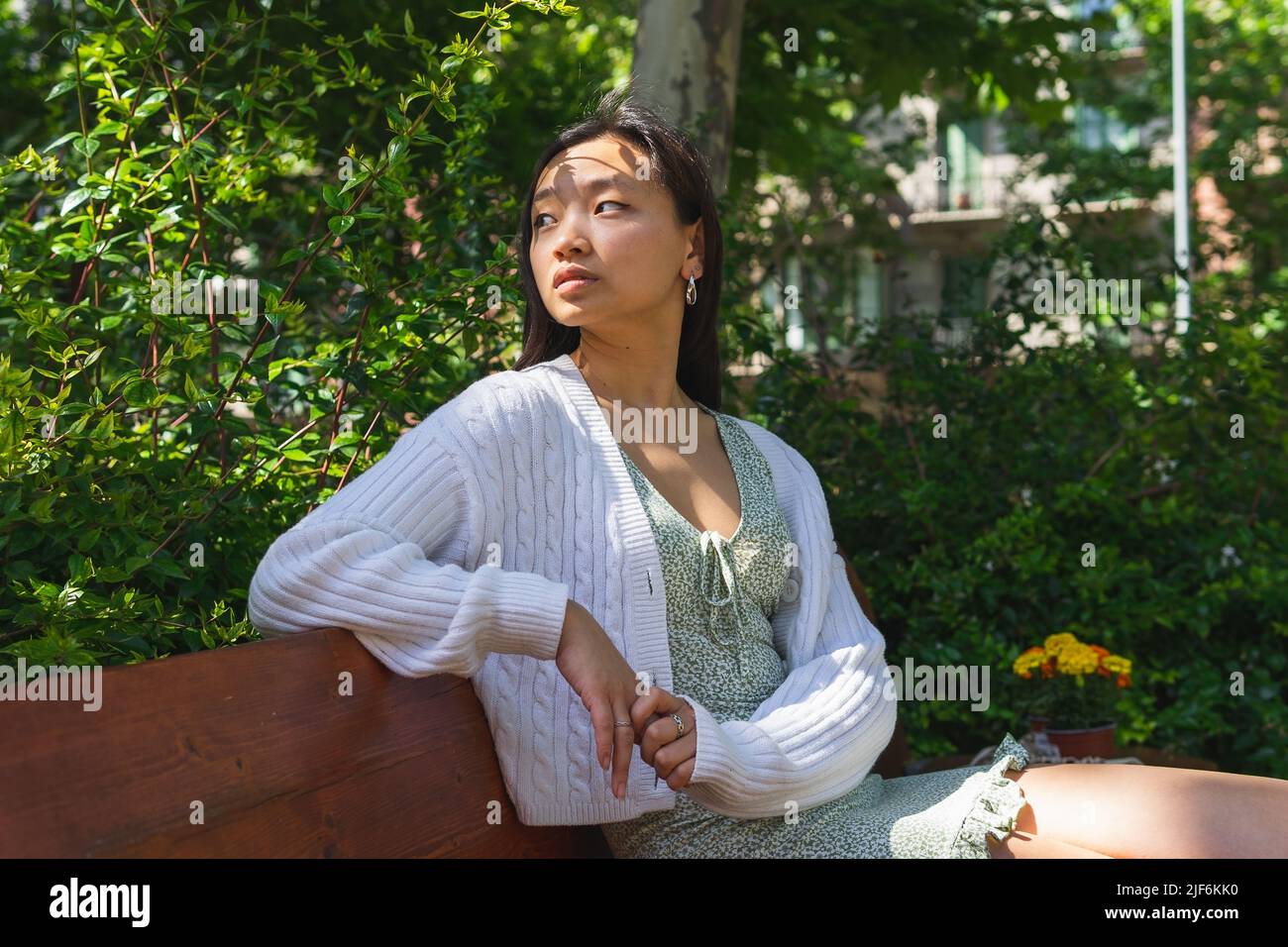 Contenuto donna giardiniere in grembiule in piedi con assortiti vasi di fiori freschi e piante a tavola a casa e guardando verso il basso Foto Stock