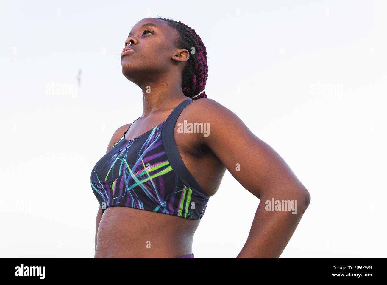 Dal basso di FIT Black atleta donna in abbigliamento sportivo riposante dopo essersi allenato contro il cielo limpido Foto Stock