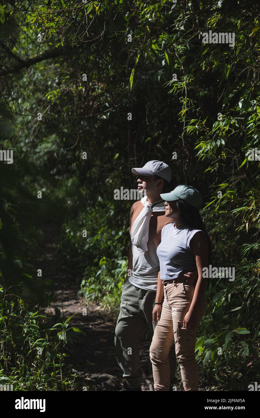 Viaggiando in coppia in abiti casual e cappellini guardando lontano mentre si levano in piedi tra alberi lussureggianti nella giungla della provincia di Pichincha durante il viaggio in Ecuador Foto Stock