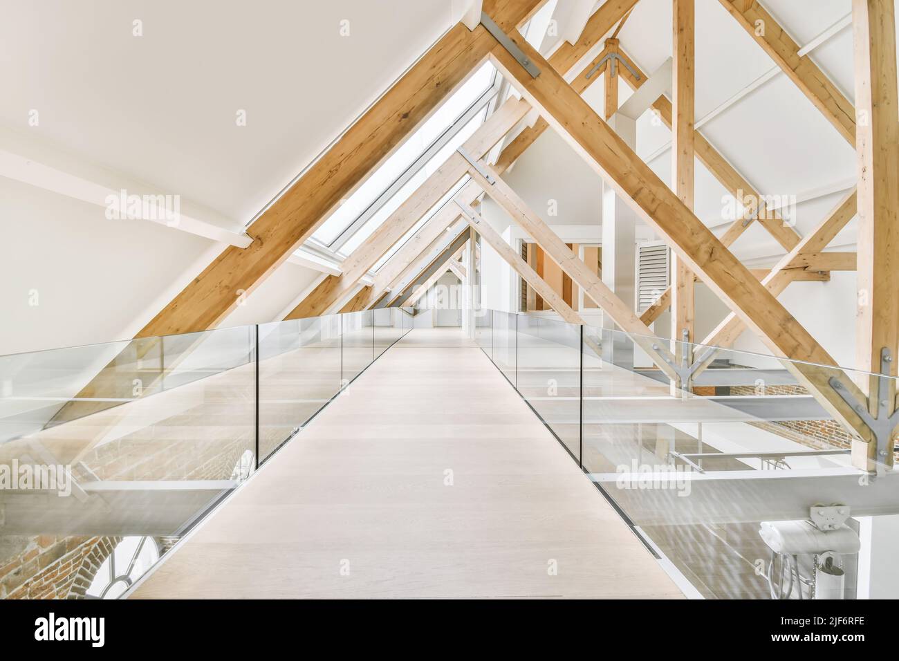 pavimento mansarda con passaggio dritto vuoto lungo una barriera di vetro e travi in legno sotto il soffitto bianco con finestre in cottage moderno chiaro Foto Stock