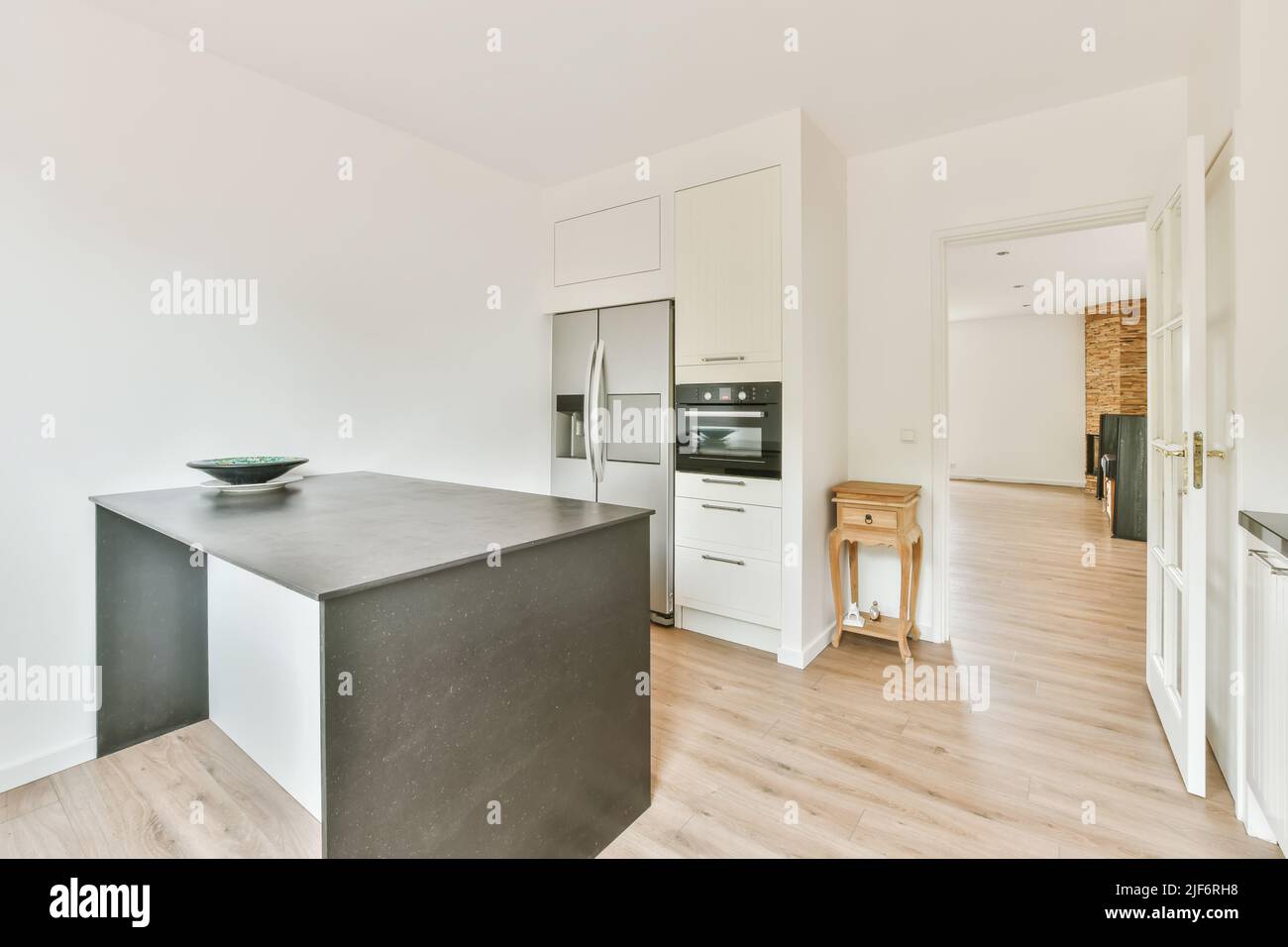 Tavolo grigio con ciotola posta in cucina chiara con armadi bianchi e moderni elettrodomestici neap aperto porta in spazioso appartamento Foto Stock