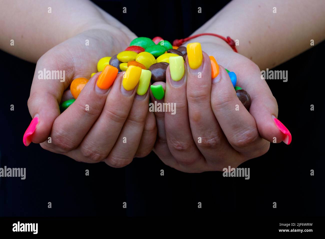 donna con le estensioni delle unghie dipinte in varietà di colori che tengono dolci colorati Foto Stock