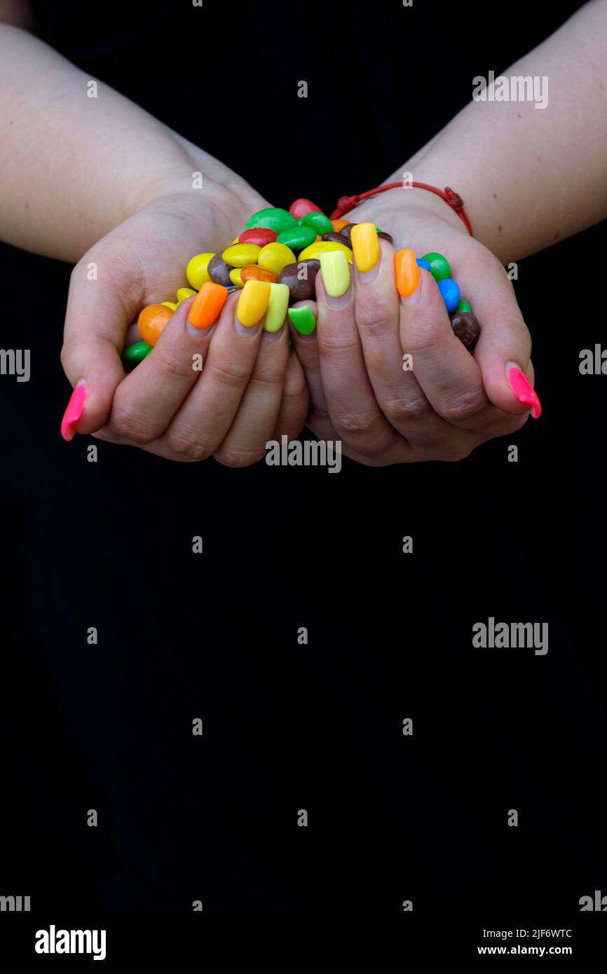 donna con le estensioni delle unghie dipinte in varietà di colori che tengono dolci colorati Foto Stock