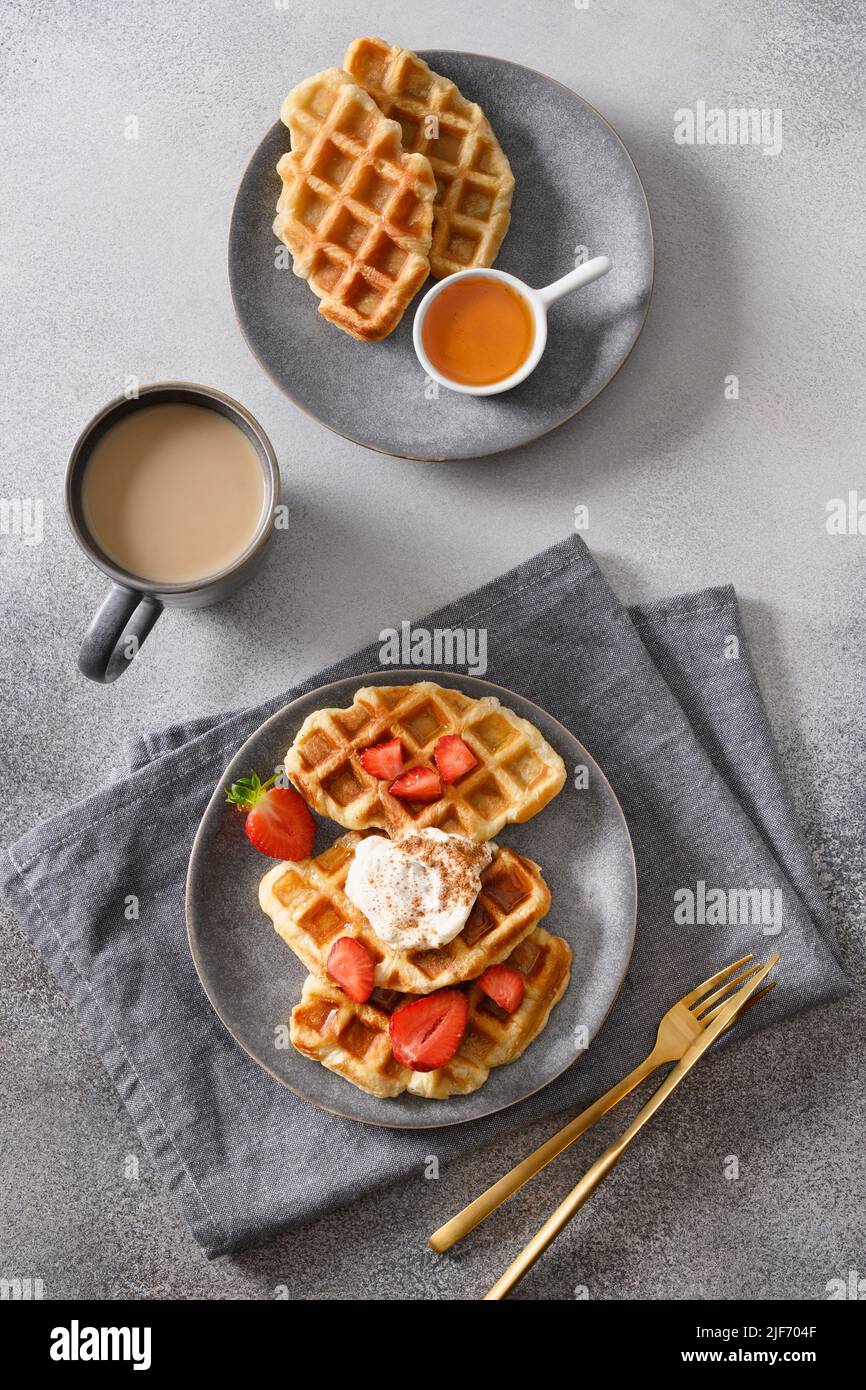 Colazione alla moda con croccanti crostini e caffè del mattino, fragole su sfondo grigio. Croissant gustoso come waffle. Vista dall'alto. Formato verticale Foto Stock