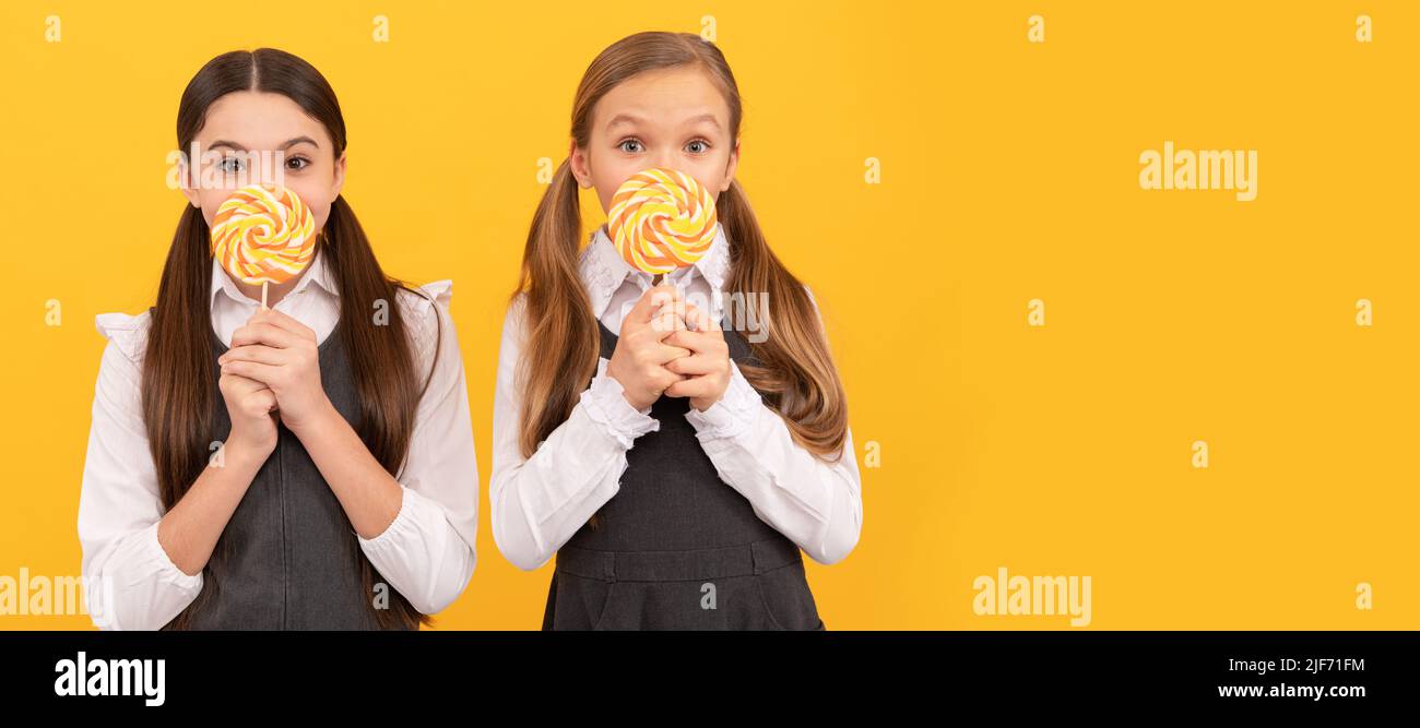 I bambini della scuola affamati tengono le lollipops colorate di swirl su sfondo giallo bastoni. Bambino adolescente con dolci, intestazione banner poster, spazio copia. Foto Stock