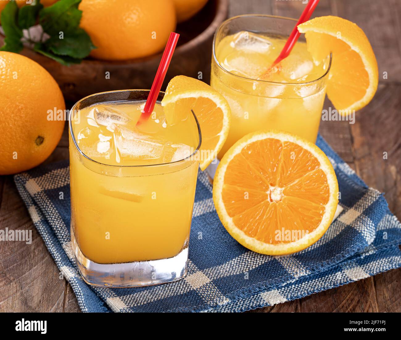 Bicchiere di succo d'arancia freddo e arance affettate su un tavolo di legno con ciotola di arance sullo sfondo Foto Stock