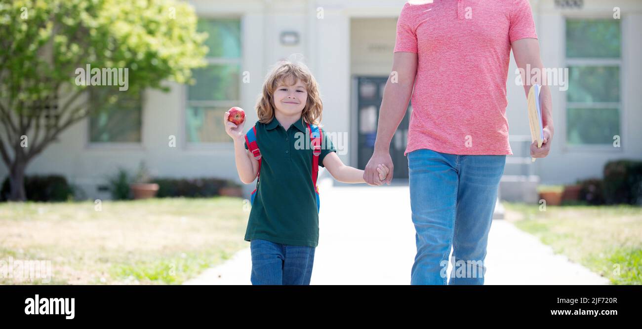 Banner di bambino di ritorno a scuola, felice famiglia di capretto e padre con mani di mela tenere che conduce al primo grado di scuola, scuola Foto Stock