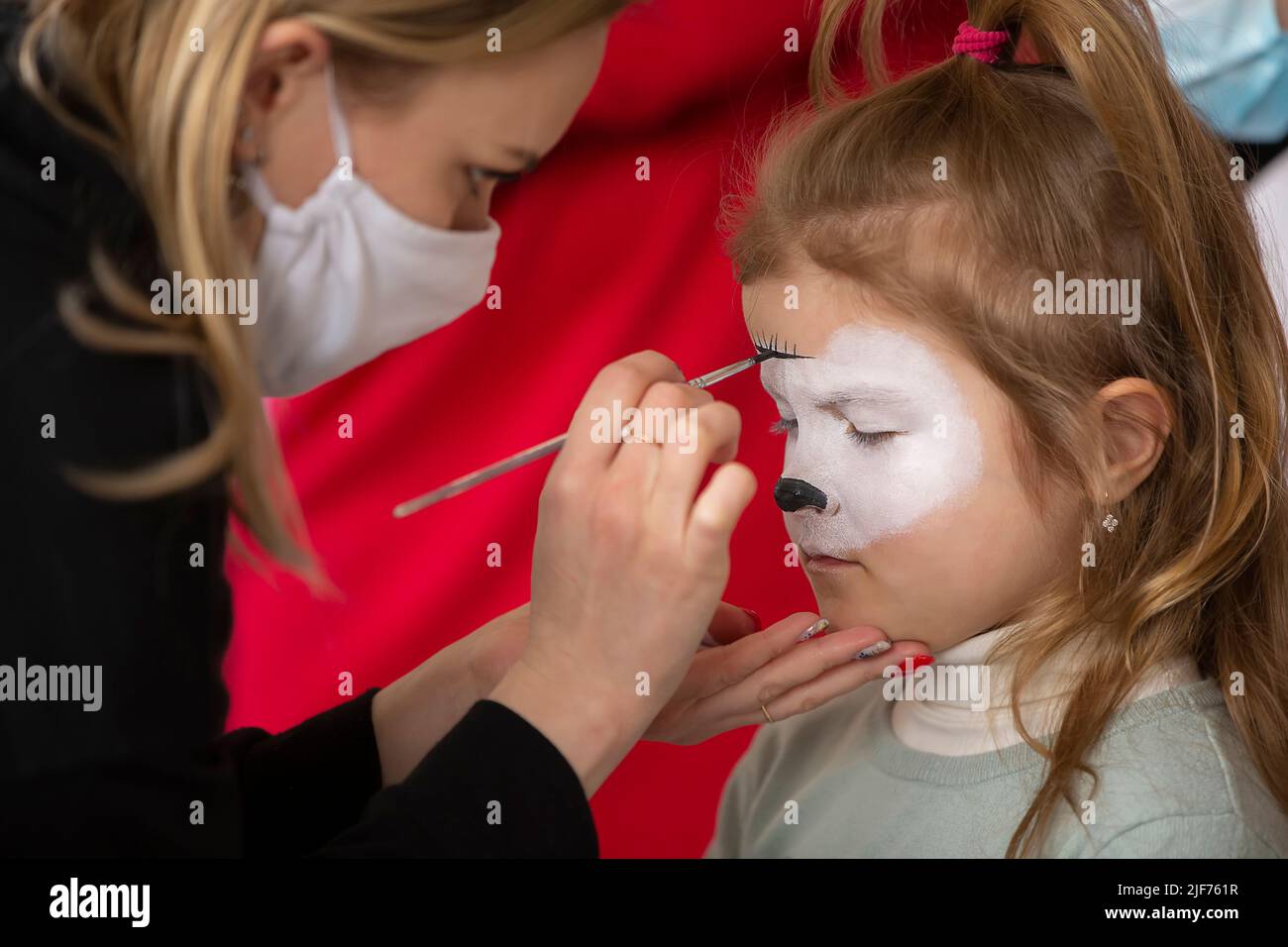 Un artista make-up disegna la pittura facciale sul volto di una bambina. Foto Stock