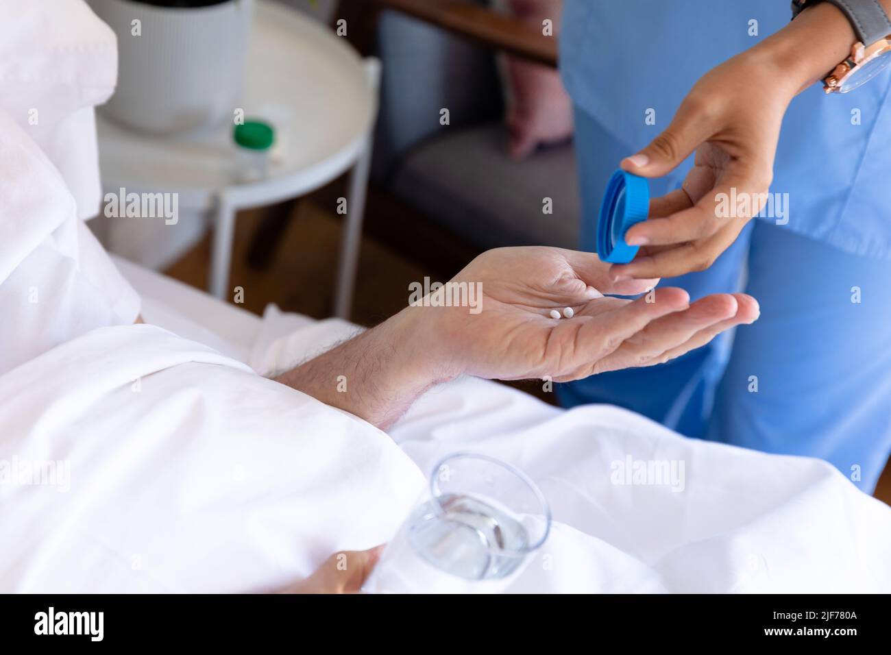 Sezione centrale dell'operatrice di salute femminile di biracial che dà le pillole mediche all'uomo anziano caucasico sul letto Foto Stock