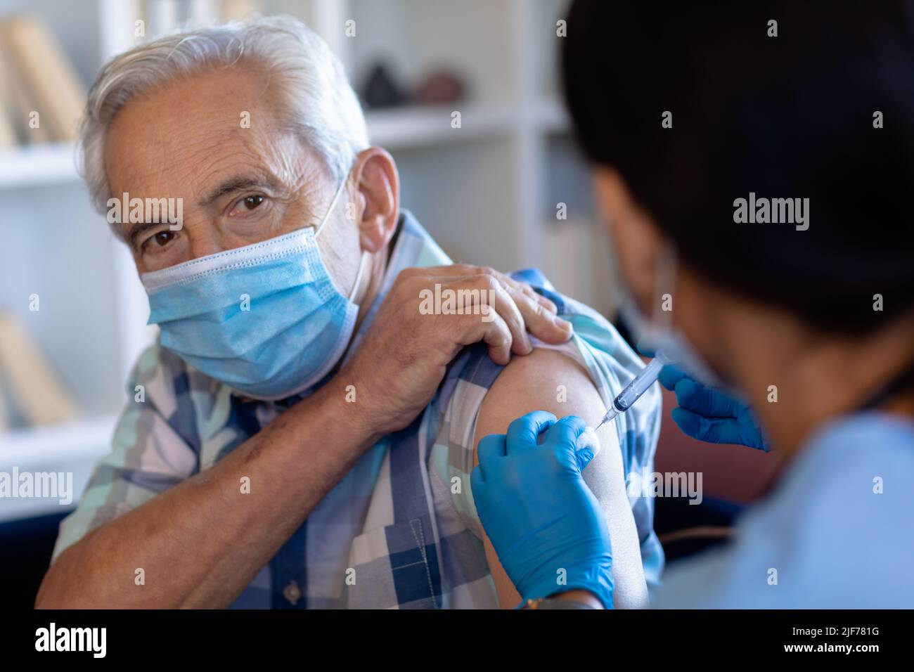 Professionista della salute femminile biracale che fa un'iniezione all'anziano caucasico a casa Foto Stock