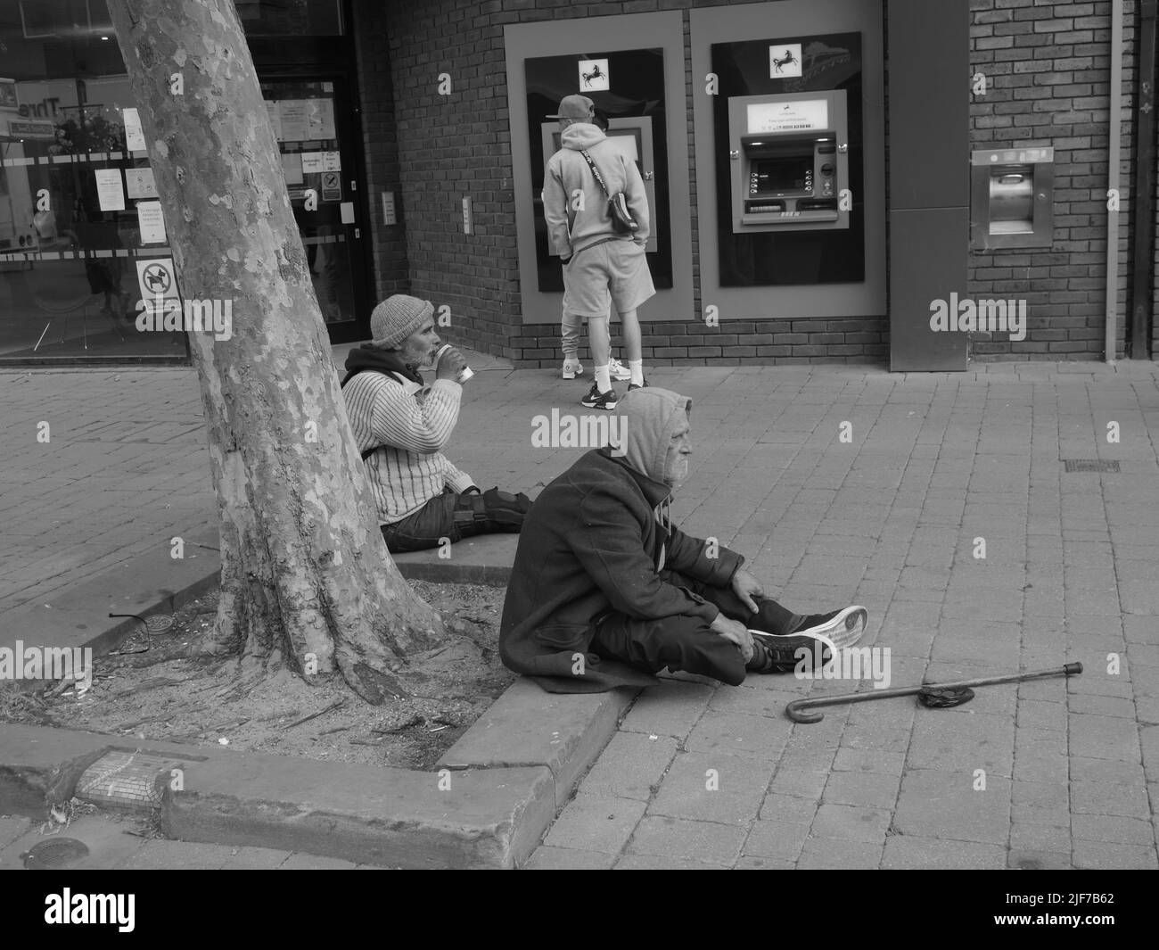 Due uomini anziani senza tetto su una strada seduta sul marciapiede Foto Stock