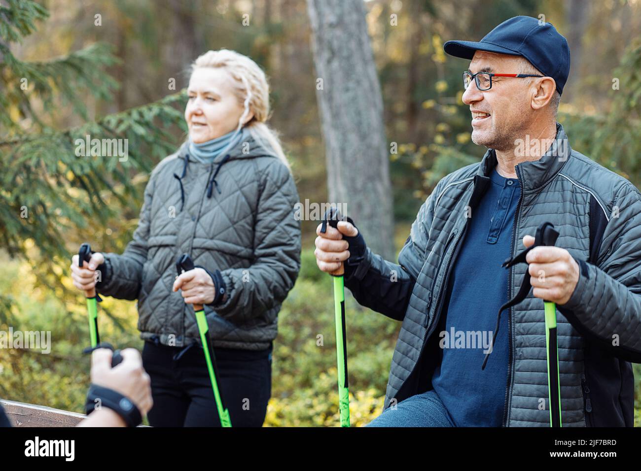 Sorridente maturo, anziani gruppo di apprendimento scandinavo, nordic walking con bastoni professionali in foresta, chiacchierando Foto Stock