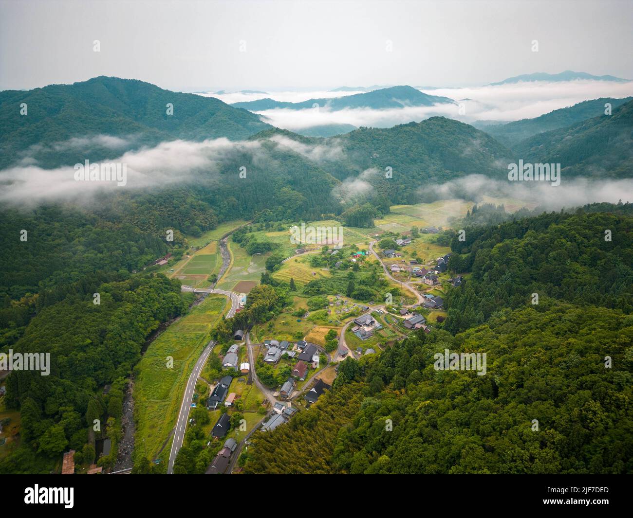 Vista aerea della nebbia mattutina sul villaggio remoto in montagne boscose Foto Stock
