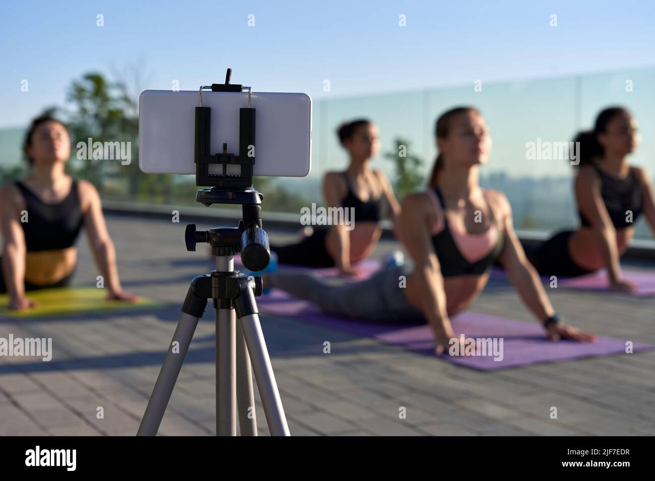 Telefono cellulare su treppiede di scatto o di streaming di gruppo yoga outdoor classe online. Foto Stock