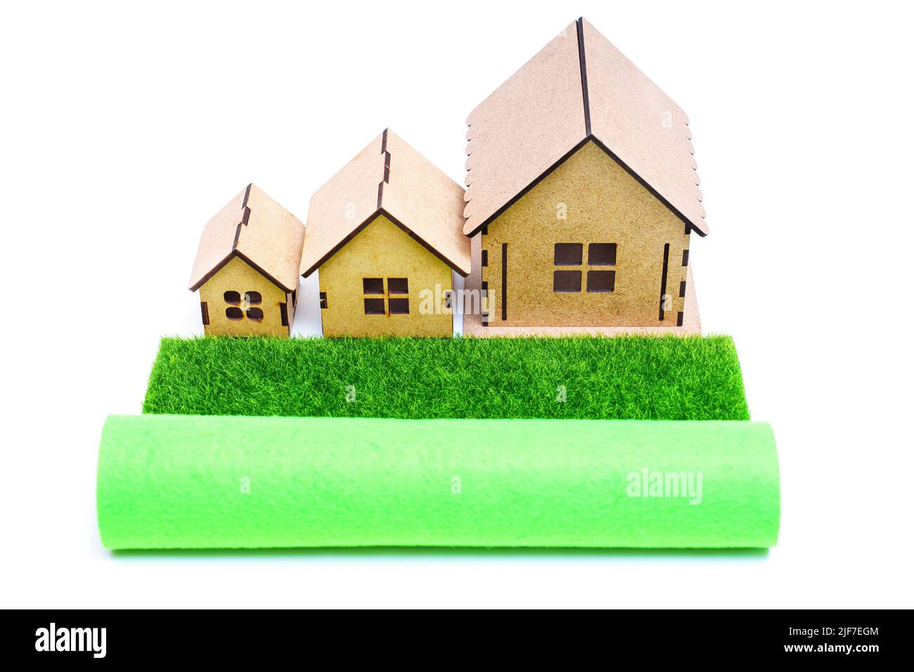 Srotolare un prato in erba artificiale di fronte a tre case giocattolo isolato su sfondo bianco. Foto Stock