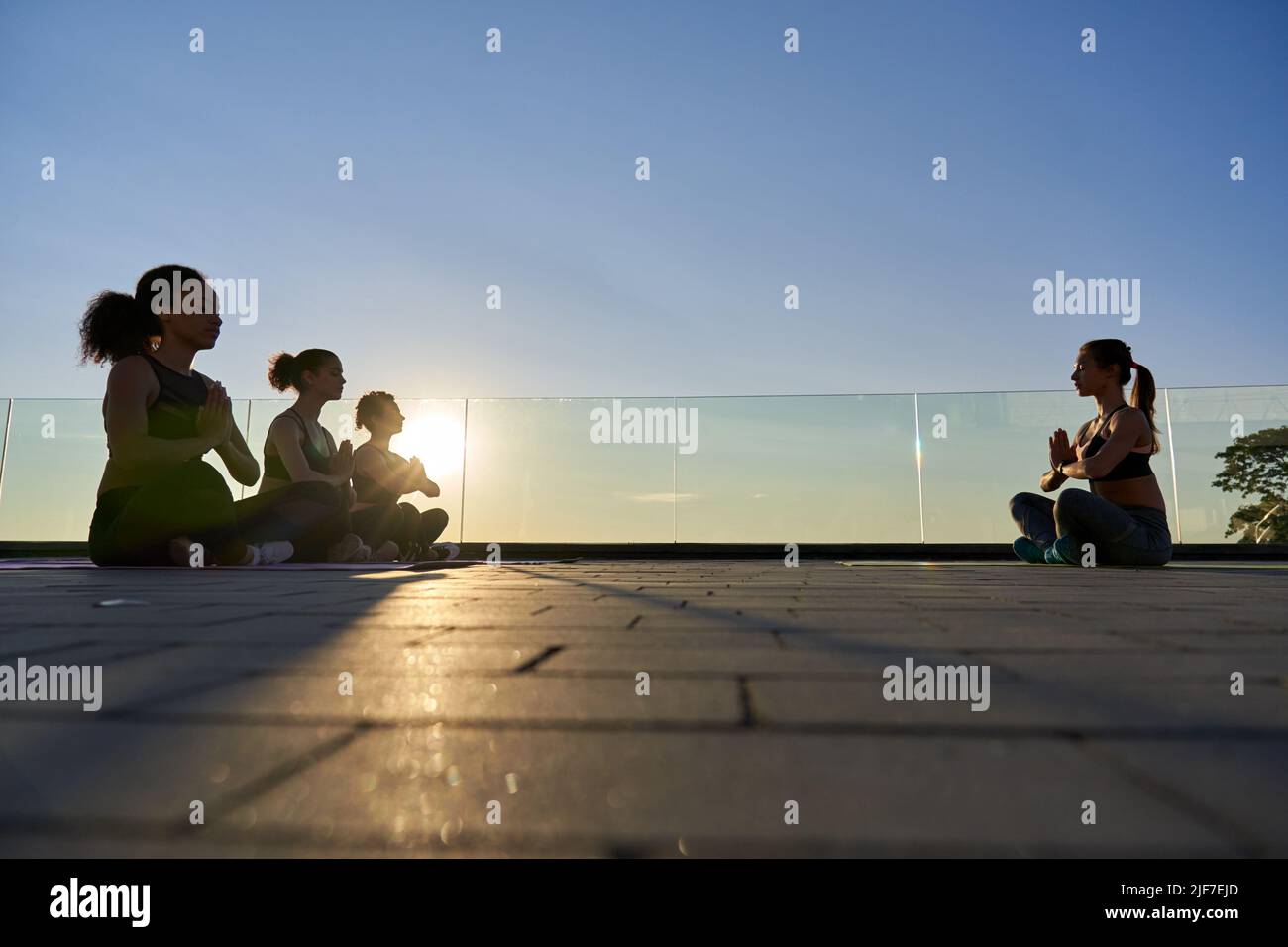 Diverse silhouette femminili e istruttore di yoga seduti all'aperto meditating. Foto Stock