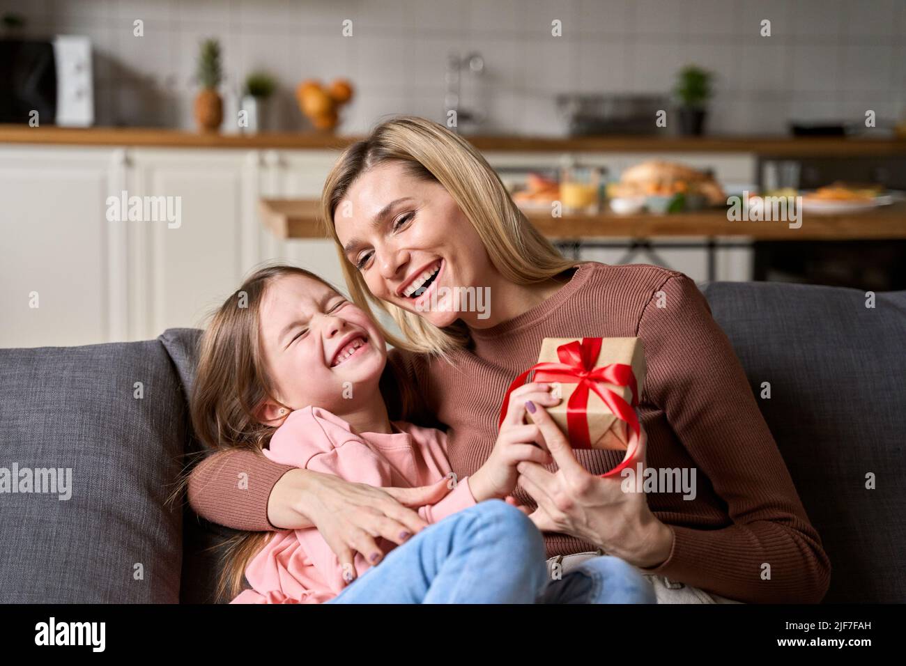 Mamma felice che riceve la scatola regalo del giorno delle madri che abbraccia la figlia del bambino nel paese. Foto Stock