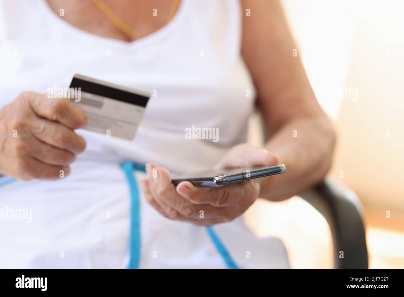 Primo piano di donna anziana con mano utilizzando uno smartphone e tenendo la carta di credito per pagare le fatture nei negozi online Foto Stock
