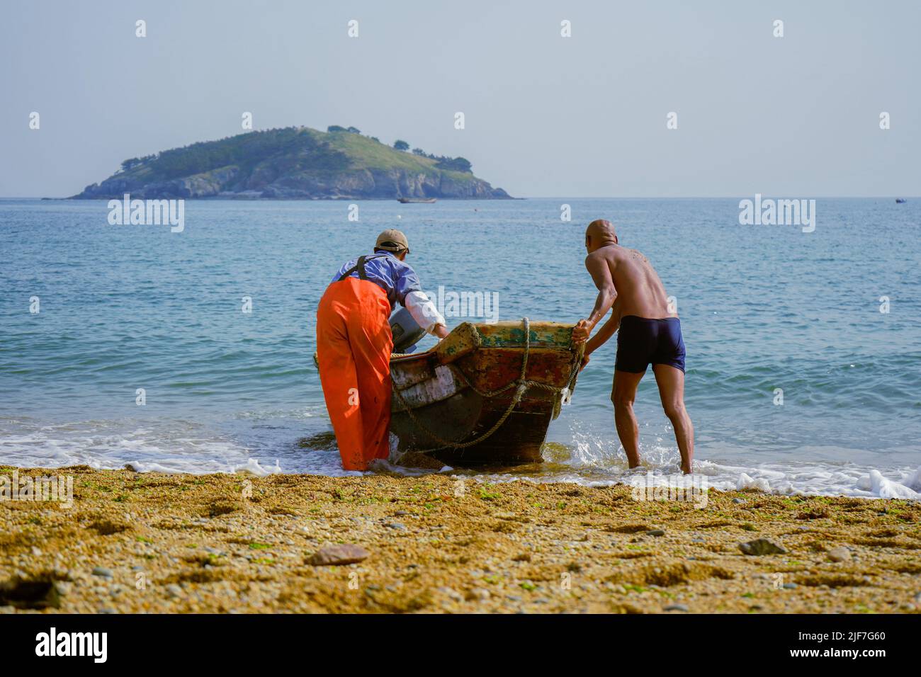 I pescatori che spingono la barca verso il mare sullo sfondo di una piccola isola. Foto Stock