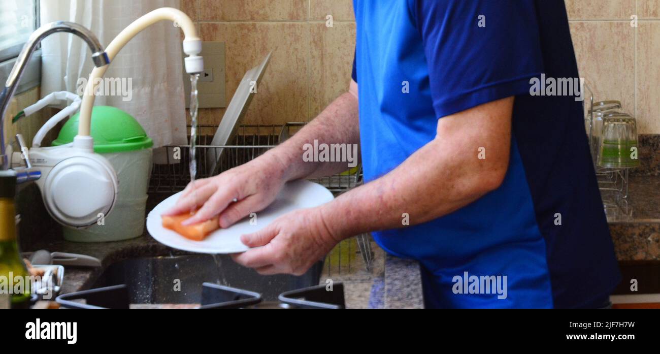 Uomo in pensione che fa lavori di casa, lavando piatti con spugna a casa, Brasile, Sud America, ritaglio intenzionale Foto Stock
