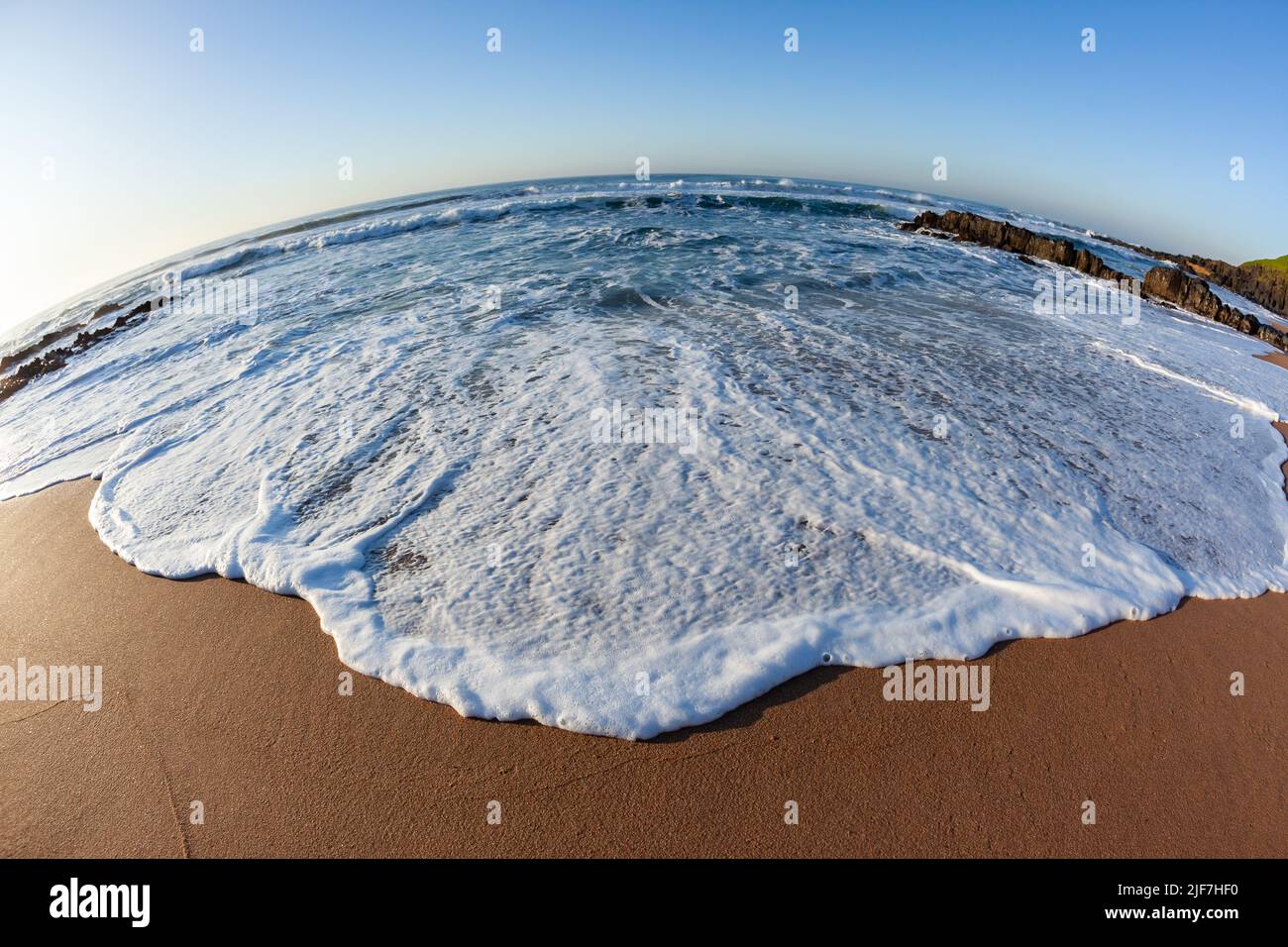 Spiaggia sabbia acque bordo onda lavare primo piano grandangolo foto lungo costa rocciosa mattina panoramico oceano orizzonte paesaggio. Foto Stock