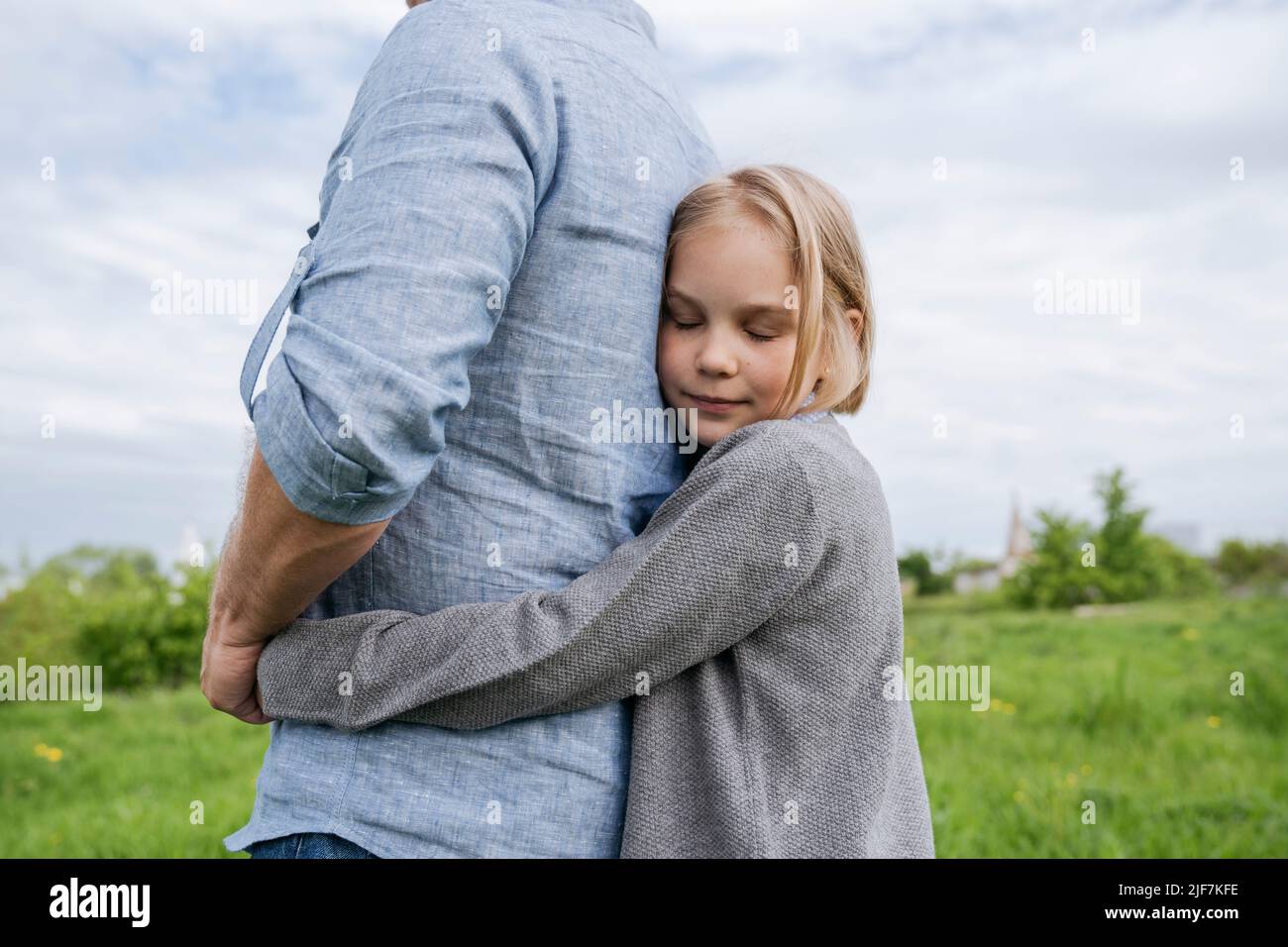 La figlia abbraccia delicatamente suo padre da dietro. Foto Stock
