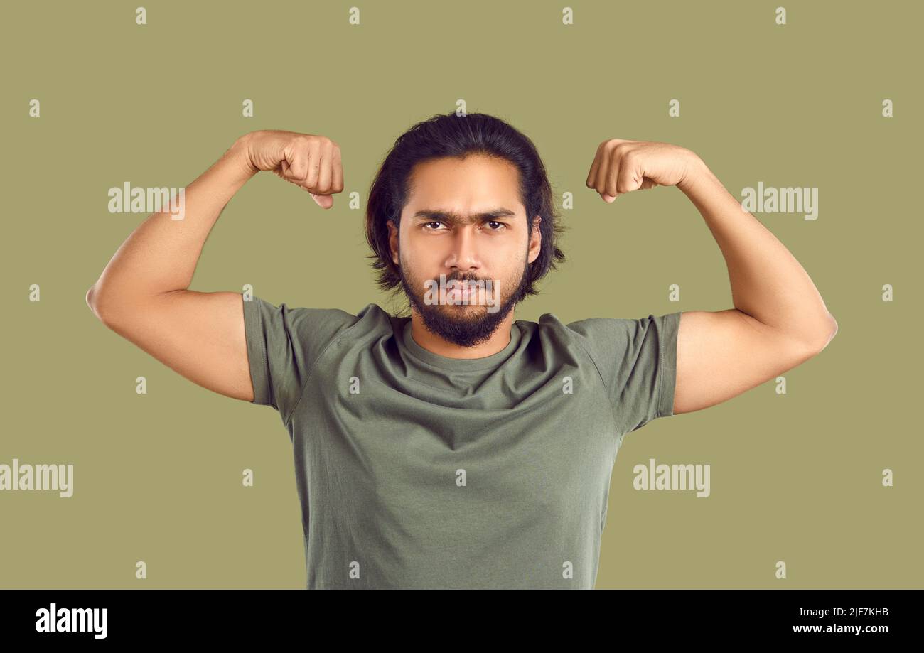 Studio ritratto di divertente serio giovane indiano uomo flettendo le braccia per mostrare la sua forza Foto Stock