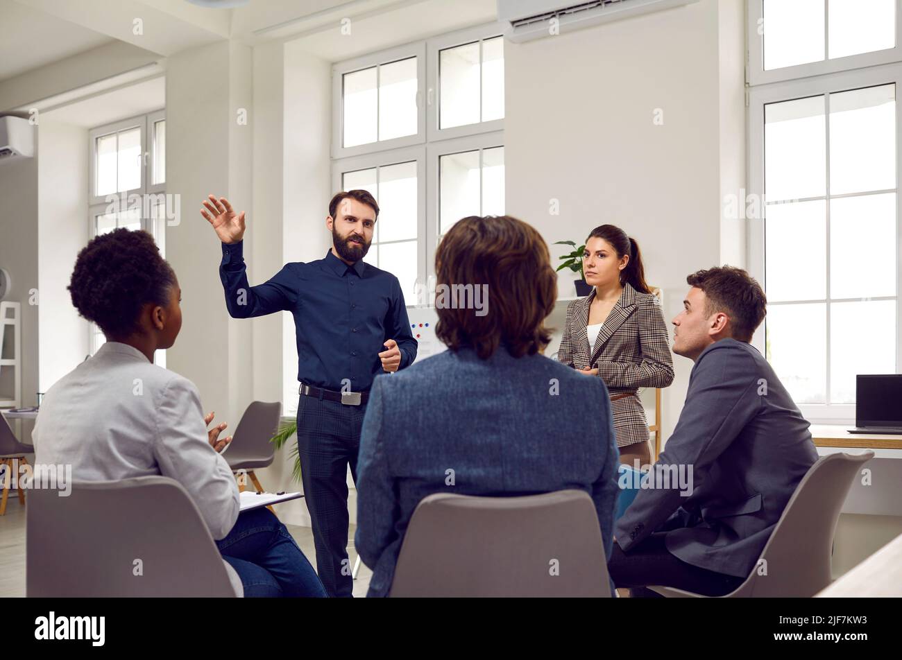 Il business coach maschile intelligente o il team leader parla con i dipendenti durante una riunione di lavoro o un brainstorming. Foto Stock