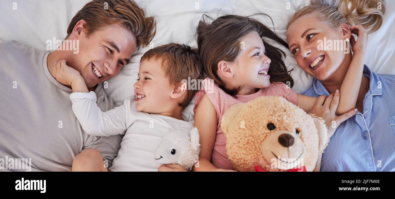 Primo piano di una felice famiglia caucasica con due bambini che si rilassano e si stendono insieme su un letto di casa, dall'alto. Piccolo fratello e sorella in attesa Foto Stock