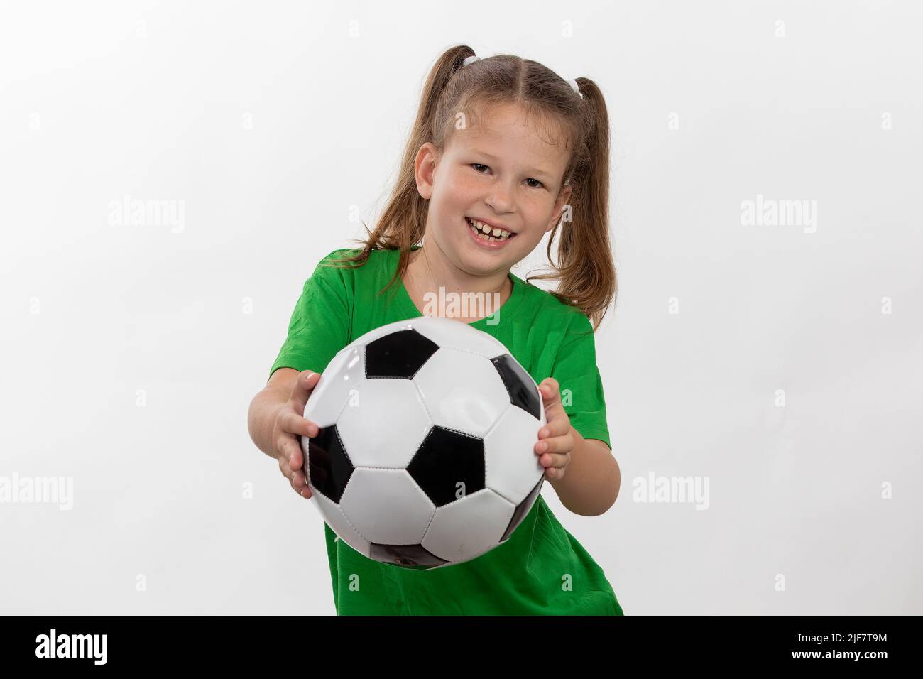 Una ragazza carina in una t-shirt verde con una palla di calcio in mano sorride isolato su uno sfondo bianco. Un bambino caucasico sportivo tiene la palla. Bambini Foto Stock