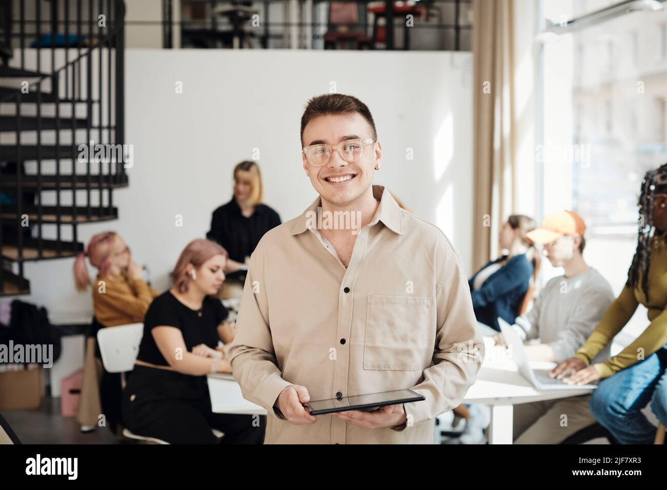 Ritratto di un programmatore maschio sorridente che tiene il tablet PC mentre si trova in ufficio Foto Stock