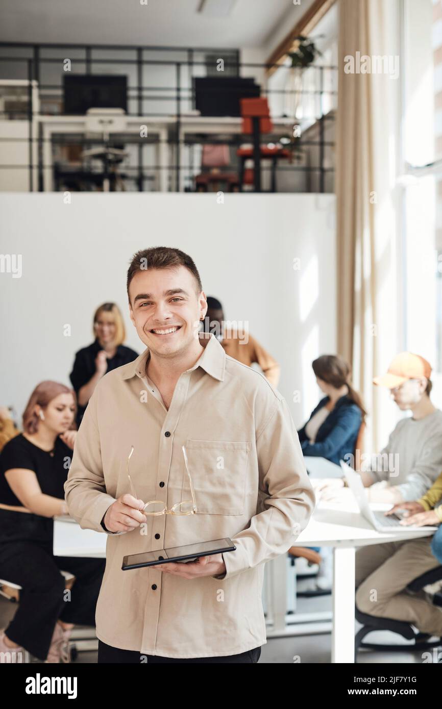 Un imprenditore maschio sorridente in piedi mentre tiene il tablet PC in ufficio Foto Stock