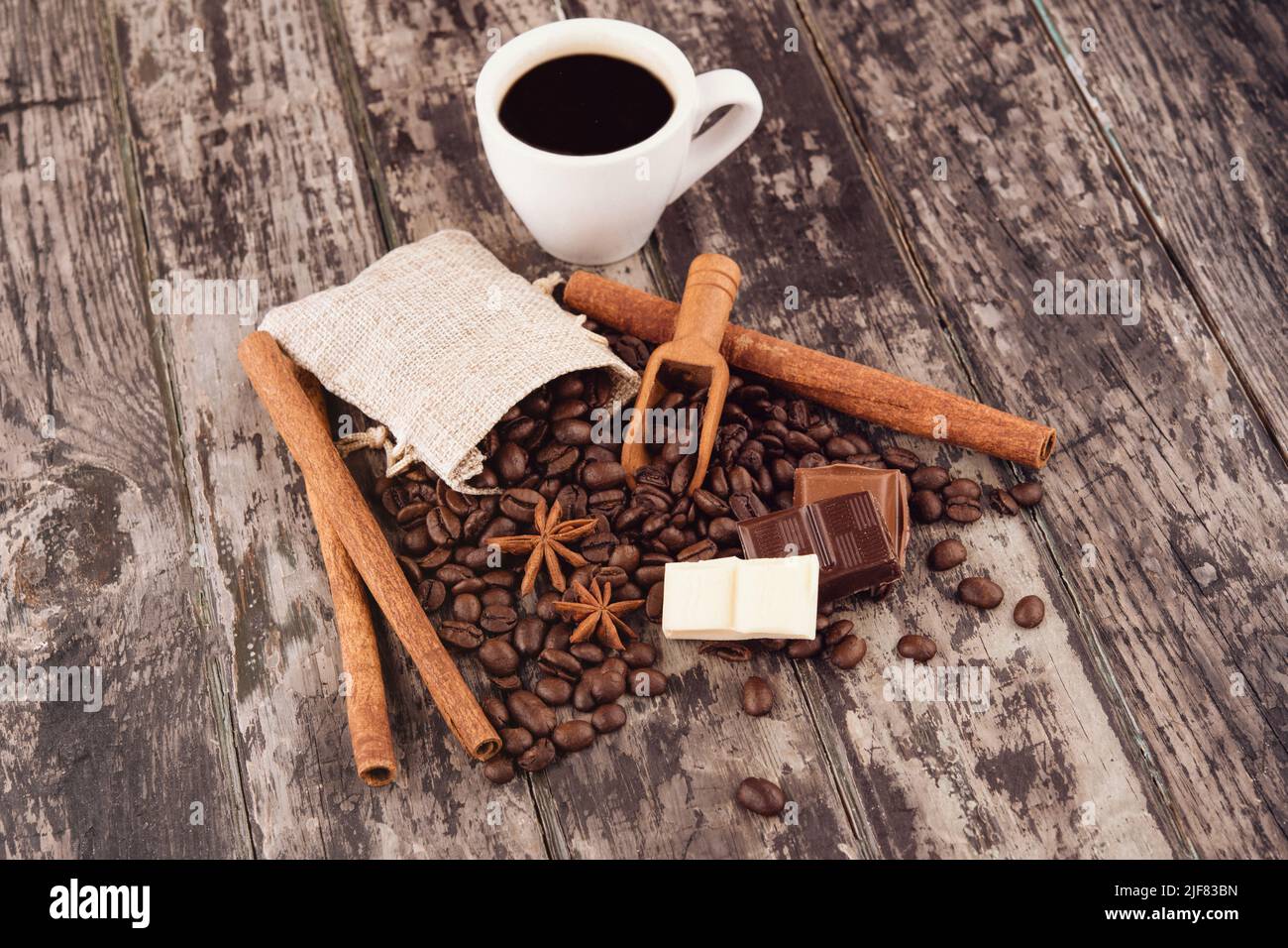 tazza di caffè con cioccolato, bastoncini di cannella e chicchi di caffè su sfondo di legno Foto Stock