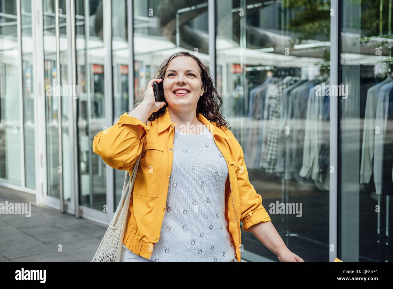 Felice sicuro sorridente più dimensione curvy giovane donna con shopping borse a piedi sulla strada della città vicino a vetrine negozio Foto Stock