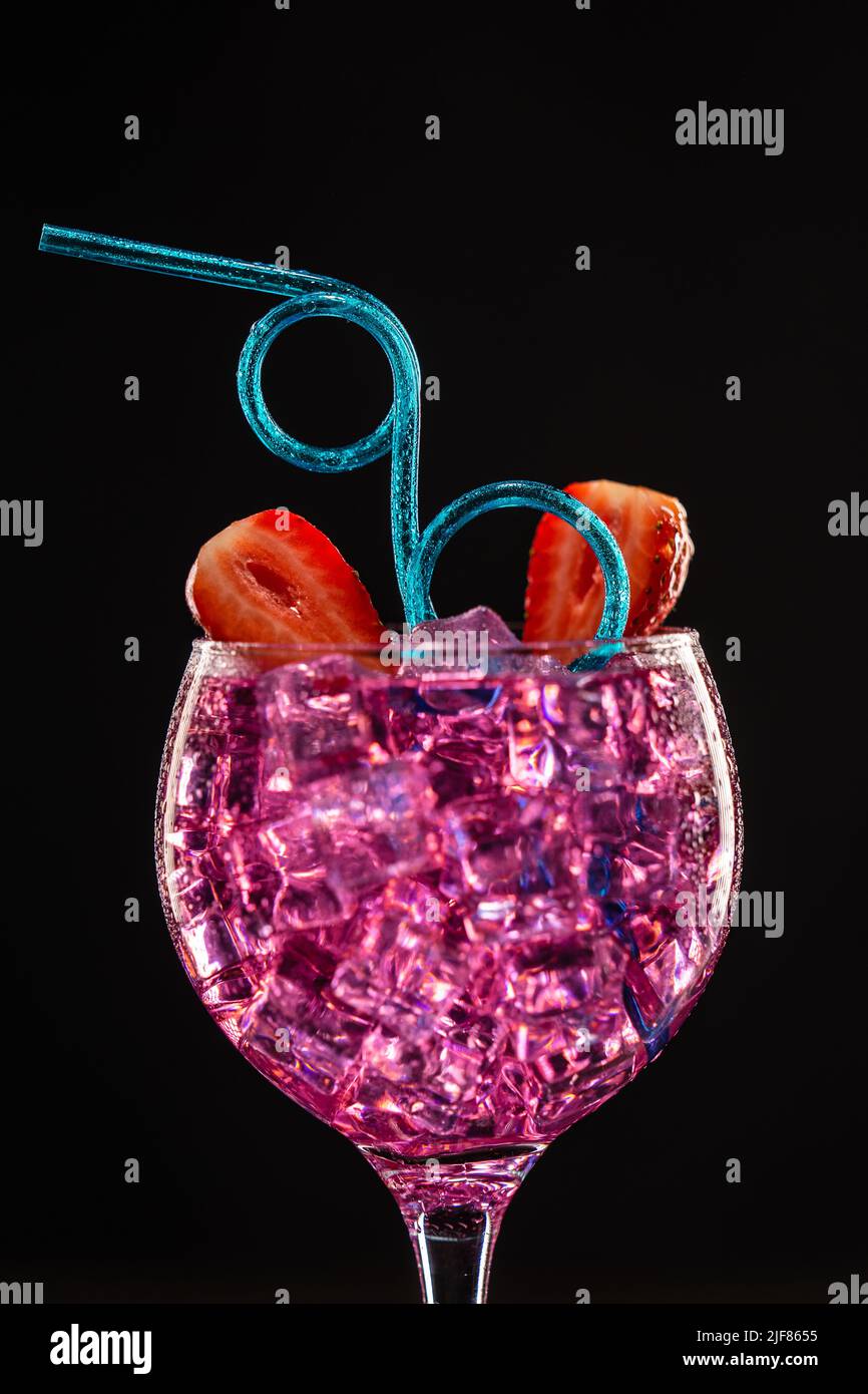Un bicchiere con un cocktail rosa pieno di ghiaccio sfondo scuro Foto Stock