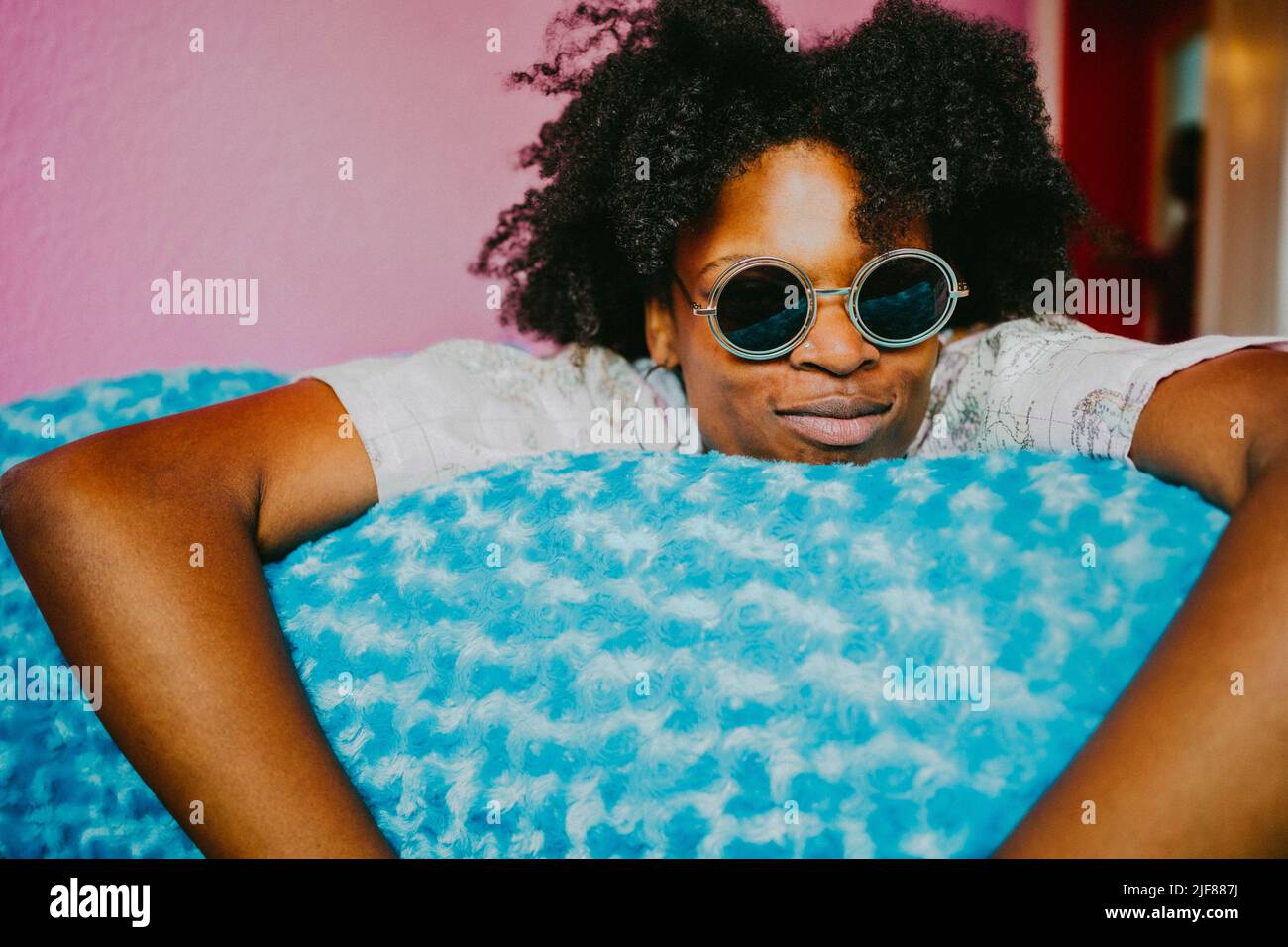 Giovane donna hipster con occhiali da sole sdraiati su coperta blu a casa Foto Stock