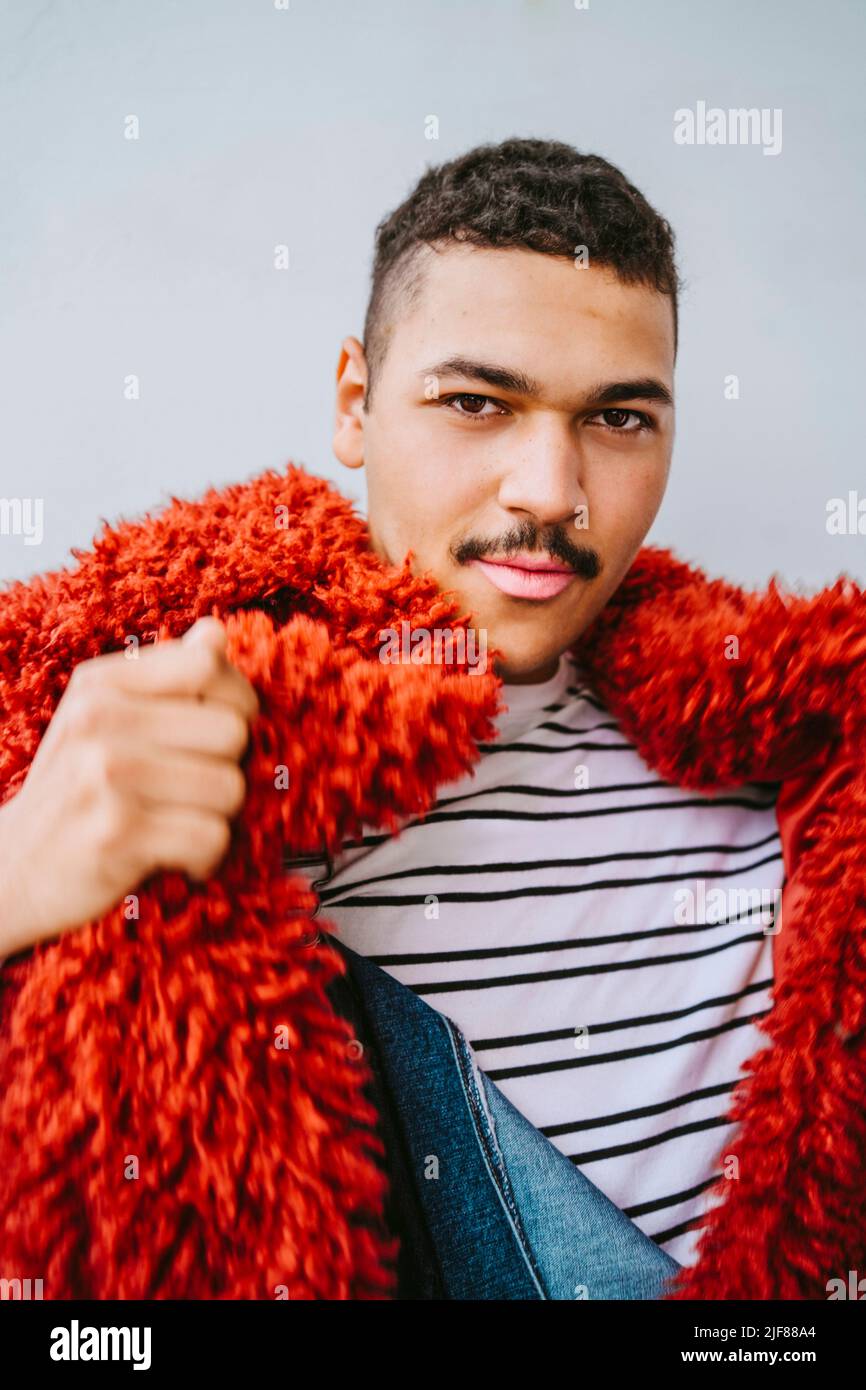 Ritratto di uomo gay con giacca in pelliccia rossa contro il muro Foto Stock