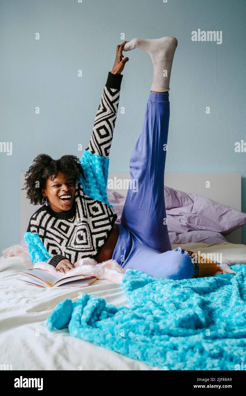 Ragazza allegra che tocca le dita dei piedi mentre si trova a letto a casa Foto Stock