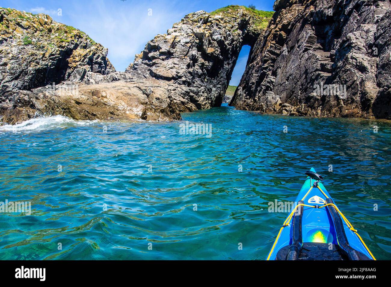 Kayak in mare attraverso un arco di roccia al largo della costa di Pembrokeshire in Galles Foto Stock