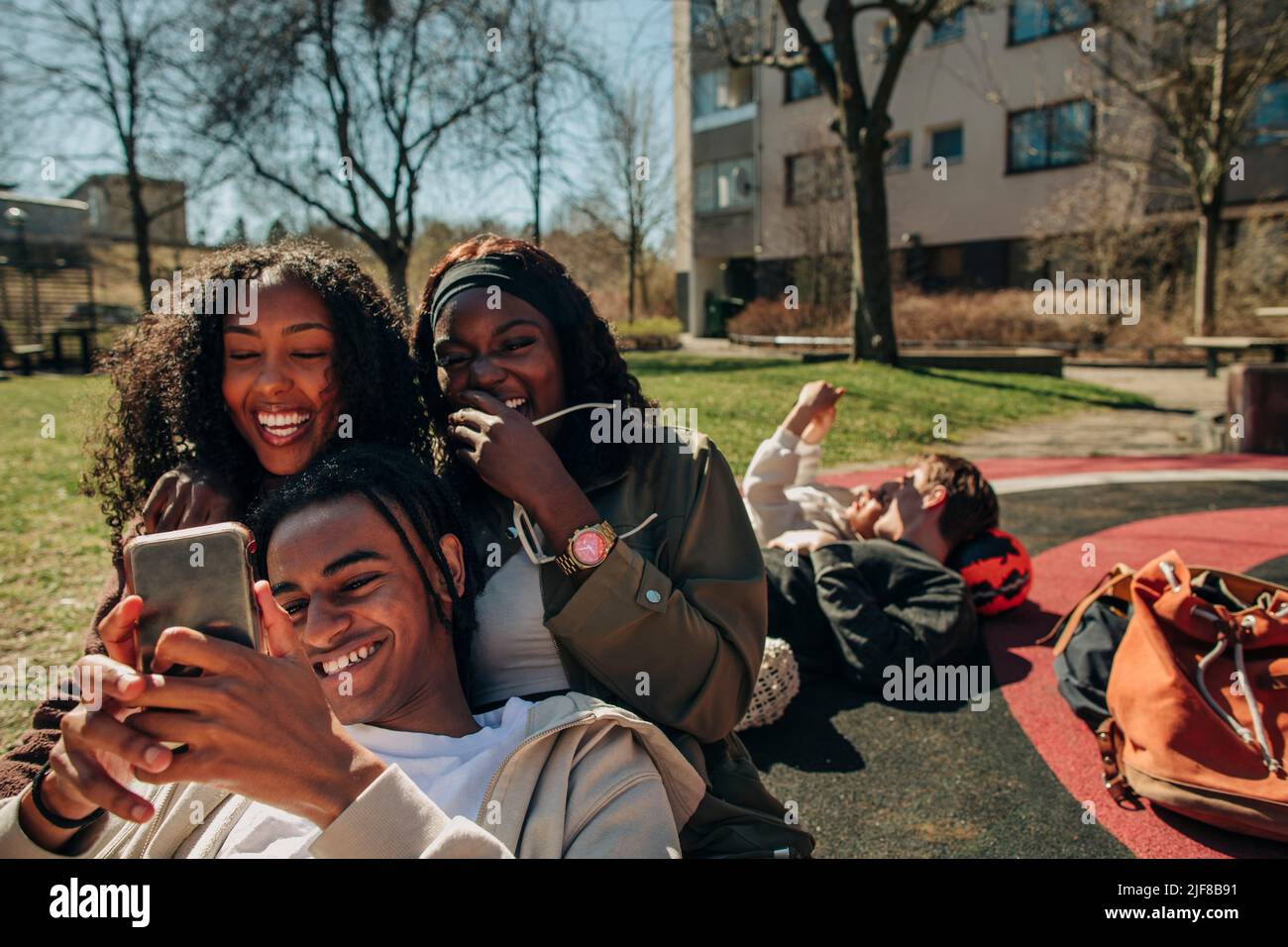 Giovani amici felici che condividono lo smartphone insieme nel parco giochi in giornata di sole Foto Stock