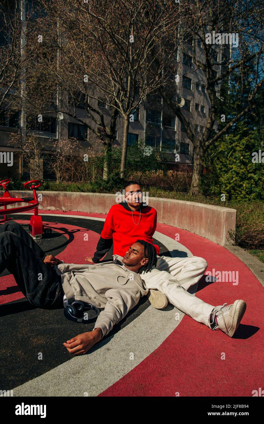 Uomo che si rilassa sul giro di un amico maschio nel parco giochi il giorno di sole Foto Stock