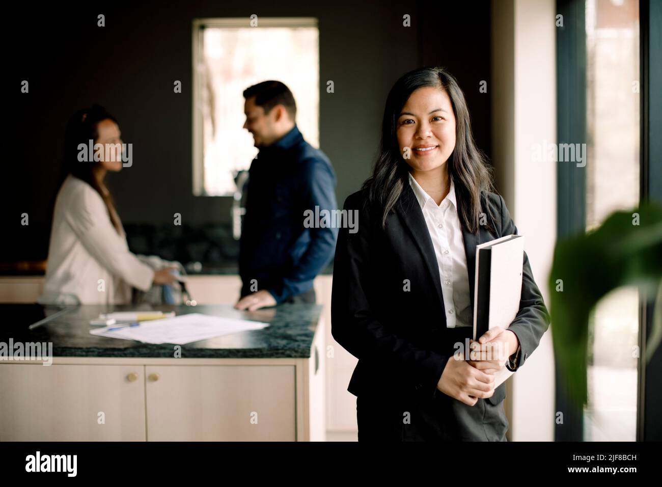 Ritratto di agente immobiliare sorridente con coppia in background a casa nuova Foto Stock