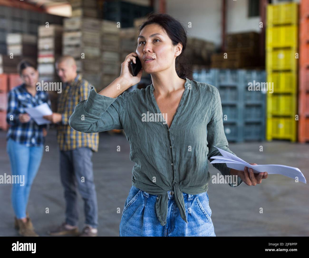 Ritratto di donna lavoratore in piedi con carte vicino casse con pesche in magazzino Foto Stock