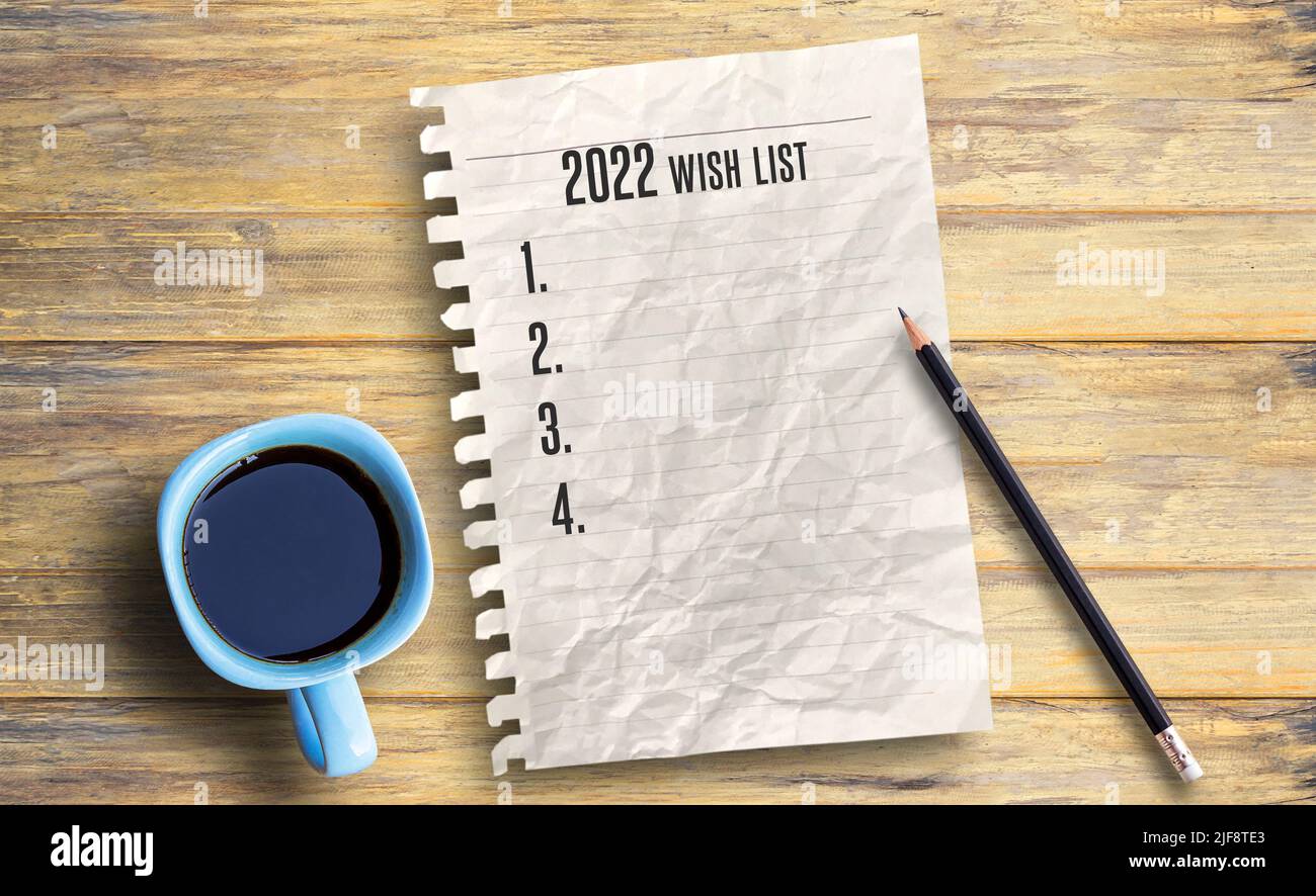Testo per 2022 wishlist e carta su sfondo tavola in legno. Tavolo da ufficio con forniture. Speranze e aspettative per il nuovo anno Foto Stock